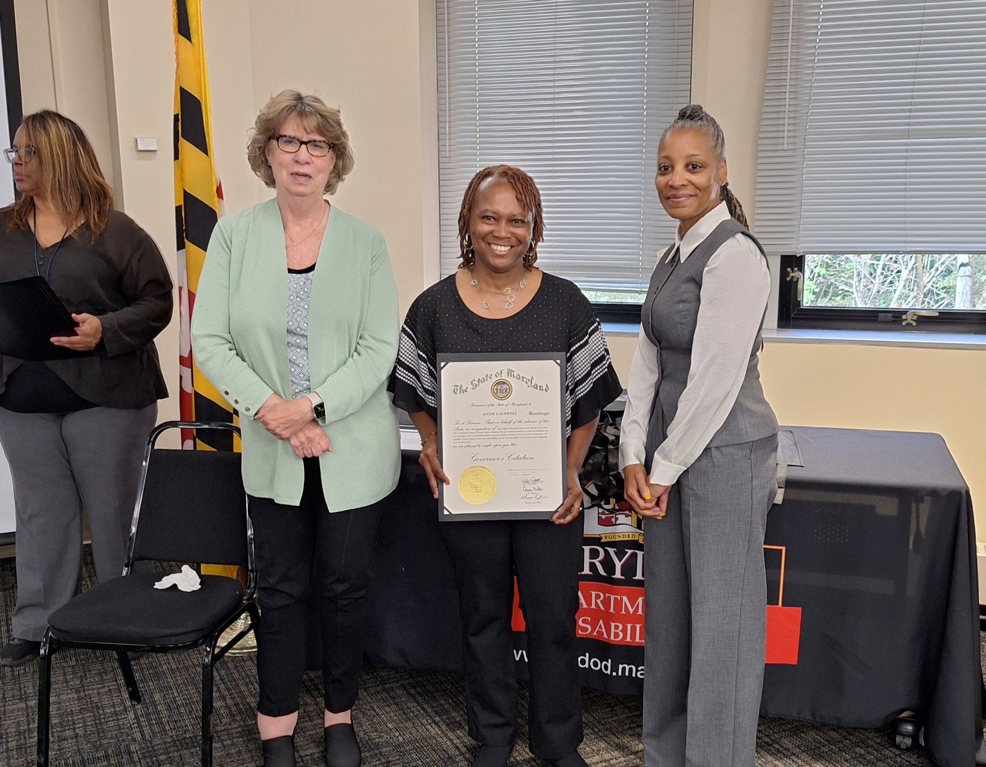 Annie holding an award certificate next to Secretary Beatty and Deputy Secretary Hutchinson.