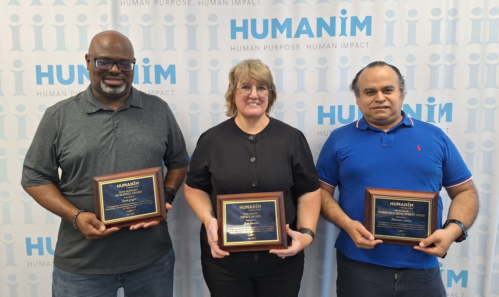 Picture of 3 people, Donte, Julie, and Abe. They are holding a plaque standing next to each other, smiling in front of a back drop with the Humanim logo